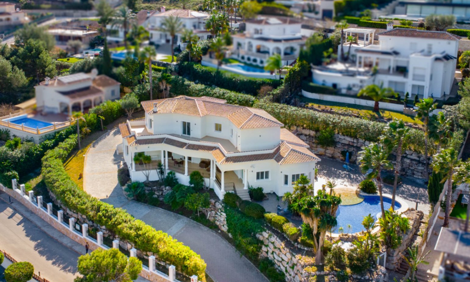 Luftaufnahme der Villa mit weißer Fassade, Terrakotta-Dach und organisch geformtem Pool, eingebettet in einen mediterranen Garten mit Natursteinmauern.