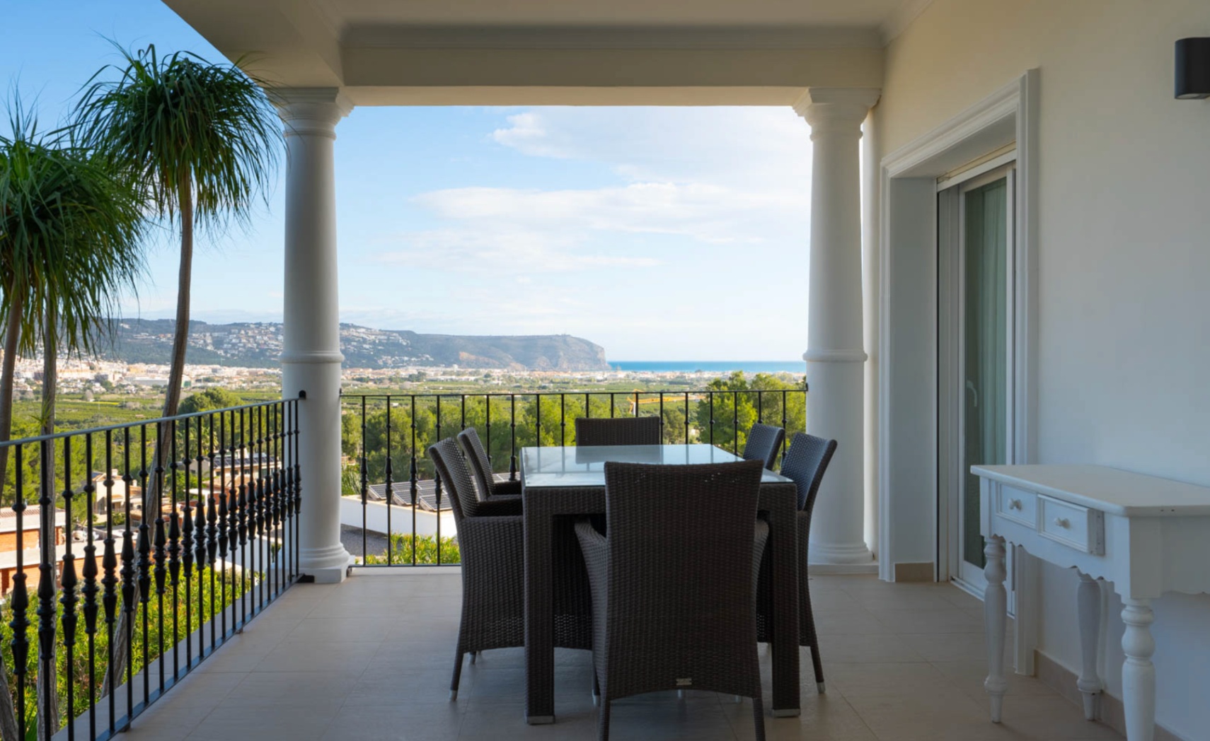 Überdachte Terrasse mit klassischen Säulen, Schmiedeeisengeländer und Essbereich mit Panoramablick auf das Tal von Jávea und das Mittelmeer.