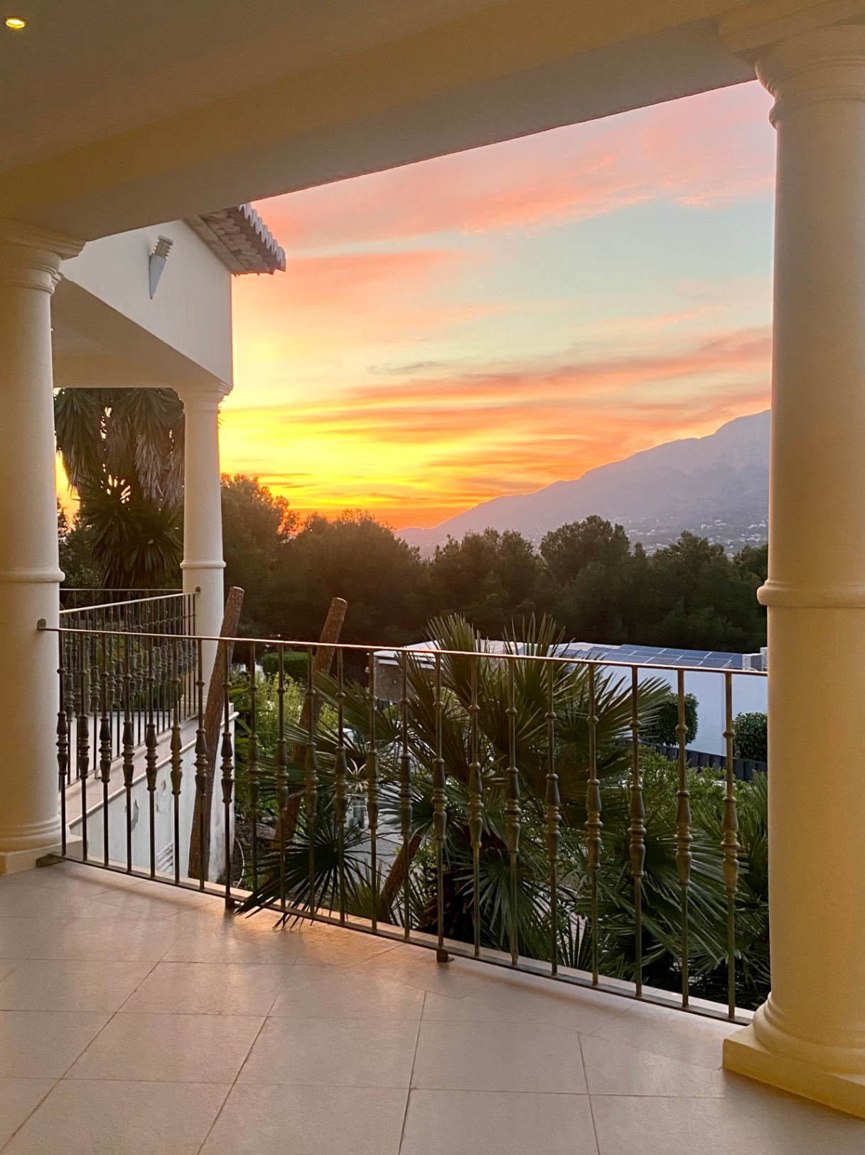 Überdachte Terrasse mit klassischen Säulen und Eisenbalustrade, die einen Panoramablick auf den Sonnenuntergang über dem Montgó und die grüne Landschaft bietet.
