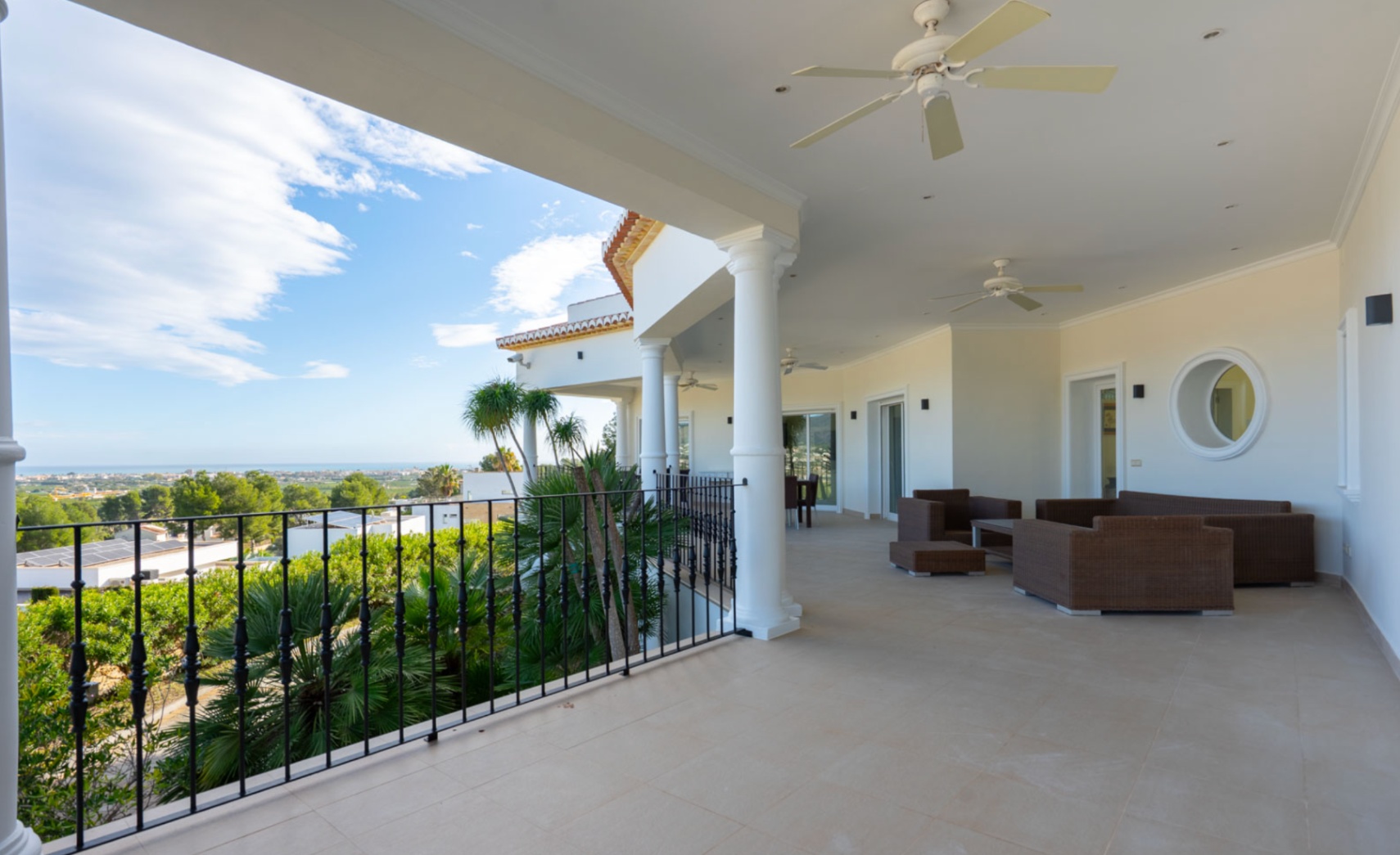 Überdachte Terrasse mit weißen Säulen, Deckenventilatoren und Loungemöbeln, mit freiem Blick auf das Mittelmeer und die Küste von Jávea.