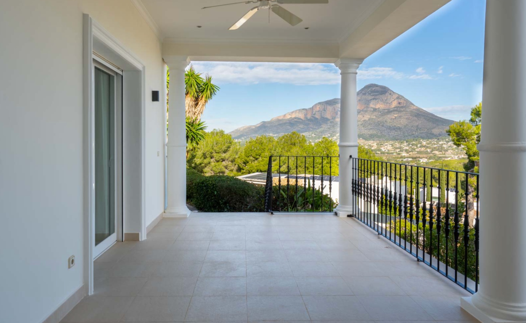Überdachte Terrasse mit weißen Säulen und Schmiedeeisengeländer, die einen freien Blick auf den Berg Montgó und die umliegende Landschaft bietet.